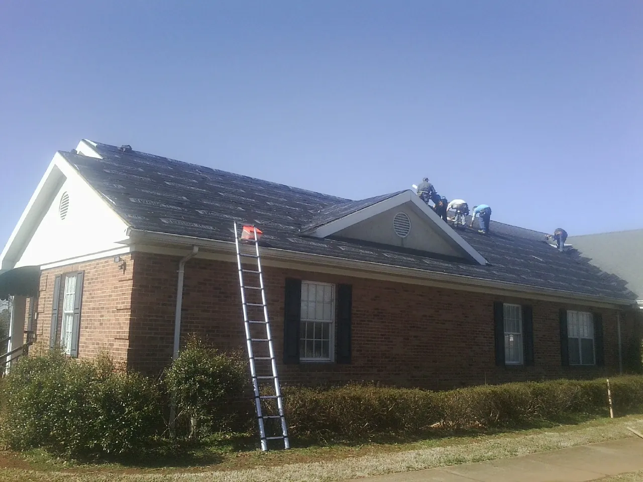 Crew tearing shingles off a brick ranch roof with a ladder set — Metal Roof Repair work by our crew in Kensal