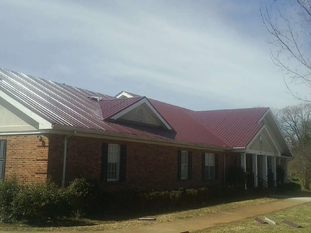 Red metal roof with gabled entries on a long brick building, from a Hail Damage Roof Repair job in Kensal