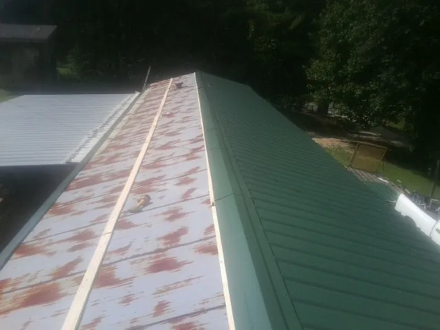 Old rusted panels beside newly installed green metal roofing — Wind Damage Roof Repair by Roofing Brothers in Kensal