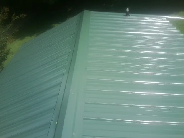New green metal panels meeting at the ridge of a roof — Flat Roof Repair work by our crew in Kensal