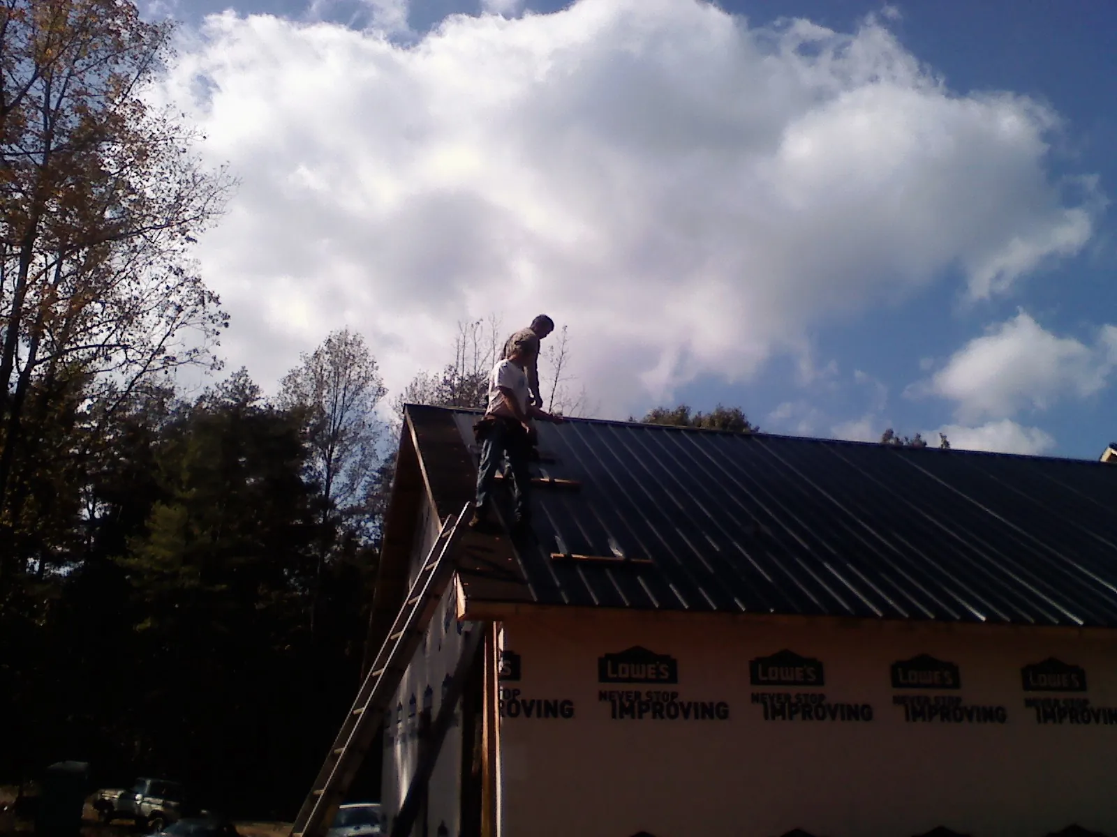 Roofer fastening dark metal panels high against a cloudy sky, from a Roof Inspection job in Kensal