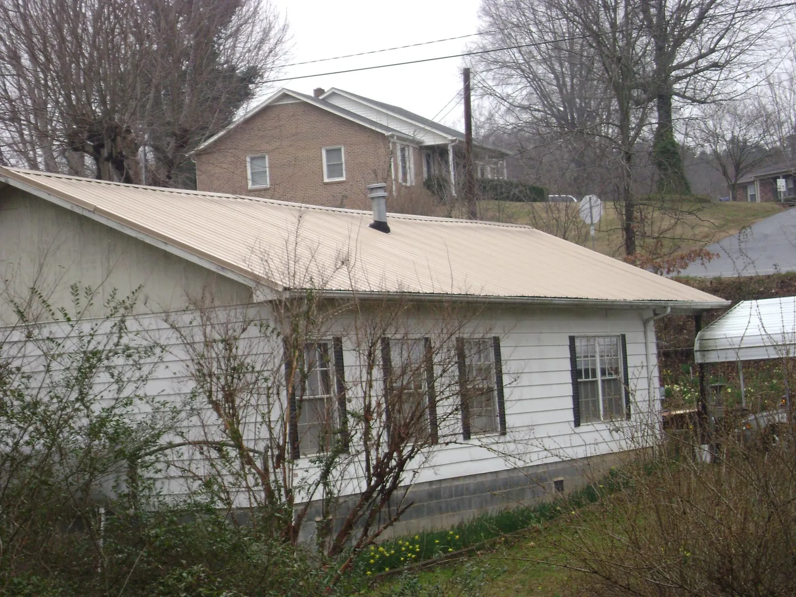 Tan metal roof on a white sided house set into a hillside — Commercial Roofing by Roofing Brothers in Kensal