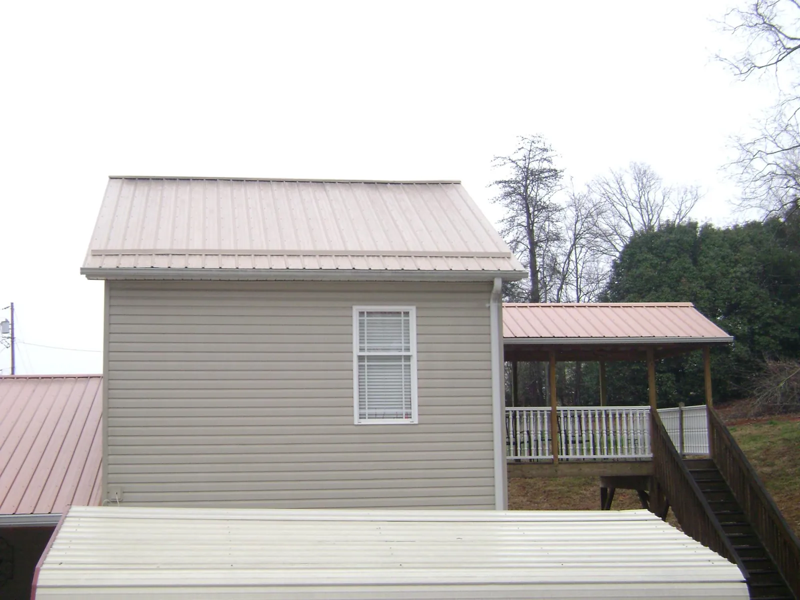 Tan metal roofs on a two story addition and attached porch, from a Roof Replacement job in Kensal